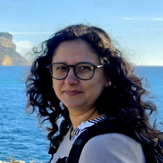 picture of Ayesha, standing in front of the ocean, wearing glasses and a backpack
