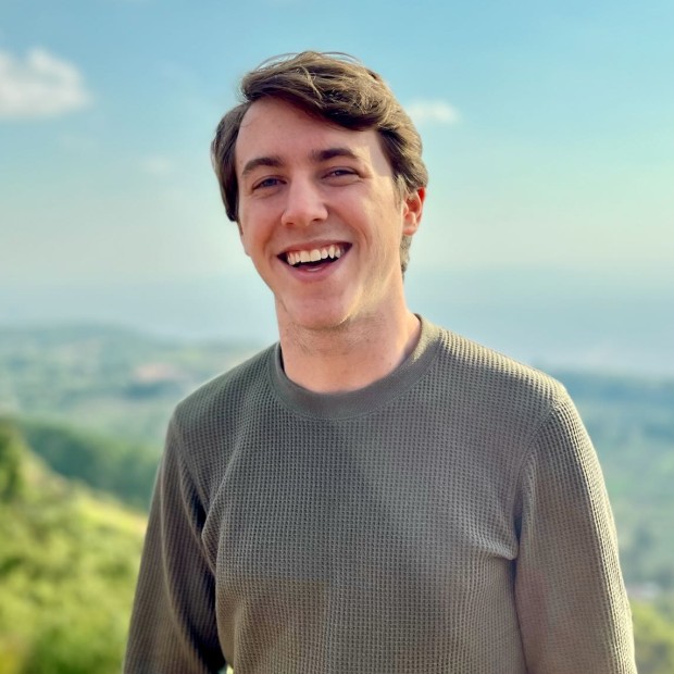 An outdoor photograph of a smiling young man with light skin and brown hair.