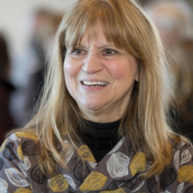 A photograph of a woman with medium-light skin and shoulder length honey-colored hair. She is wearing a brown patterned top.