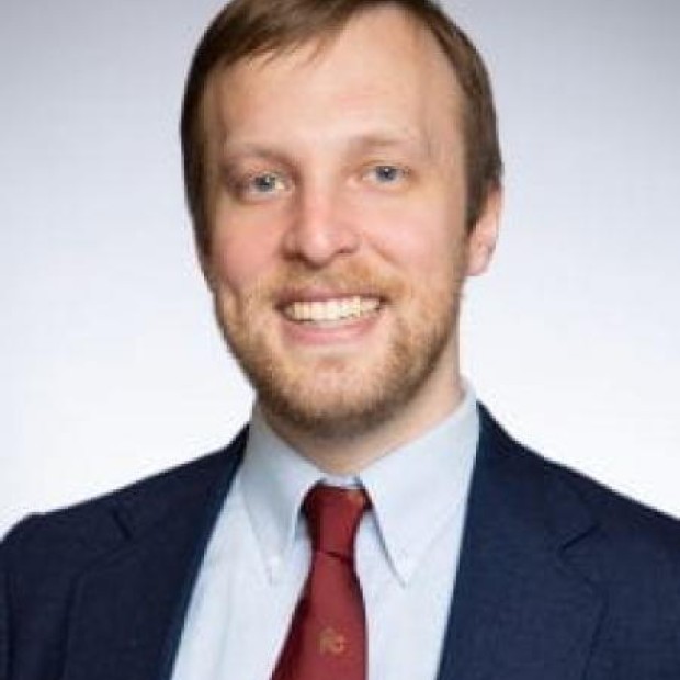 picture of Corey, wearing a blue blazer and red tie, smiling