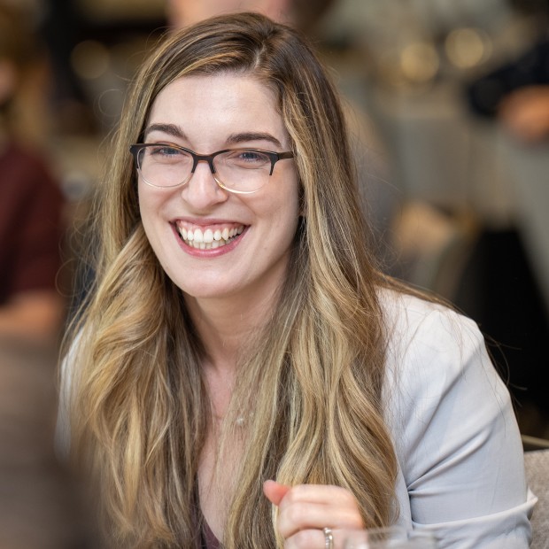 A candid photograph of a light-skinned woman with long blond hair and glasses. She's smiling.