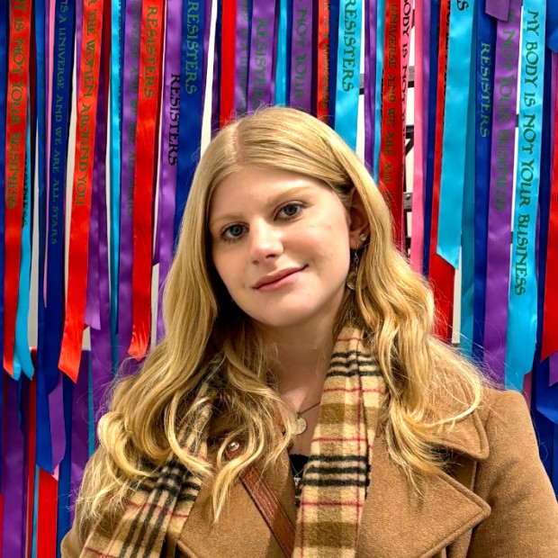 picture of Lia, wearing a coat and scarf, standing in front of a colorful piece of art