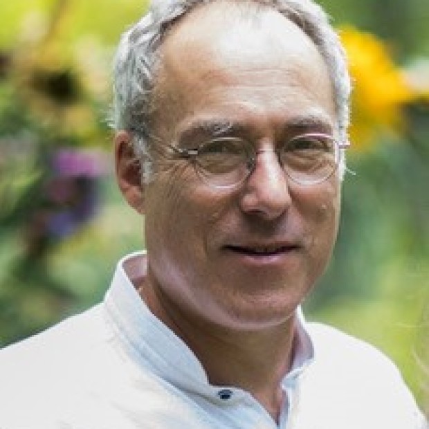 A professional headshot of a man with medium-light skin smiling slightly at the camera. 