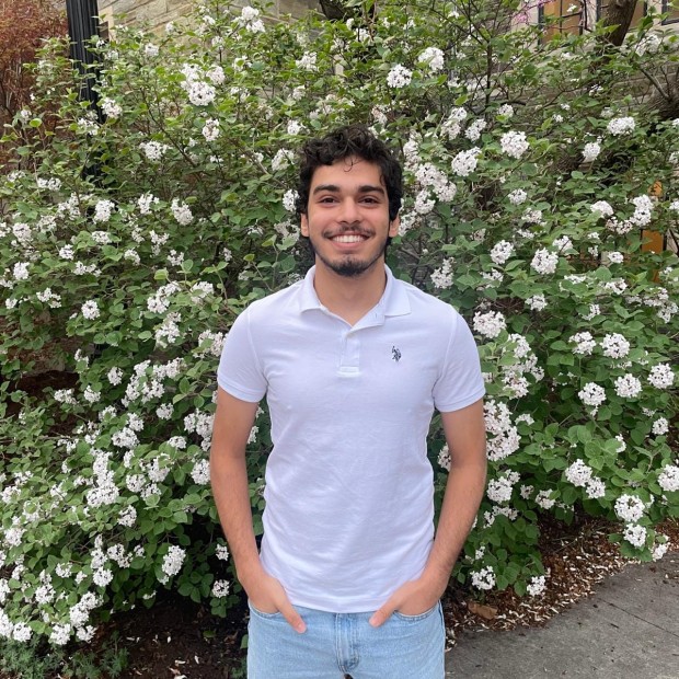 picture of Mohammad Labadi, wearing a white shirt and standing outside, in front of a flowering tree 
