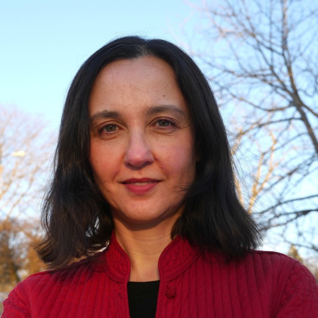 An outdoor photograph of a woman with medium-light skin and dark hair. she's wearing a black shirt and red jacket.