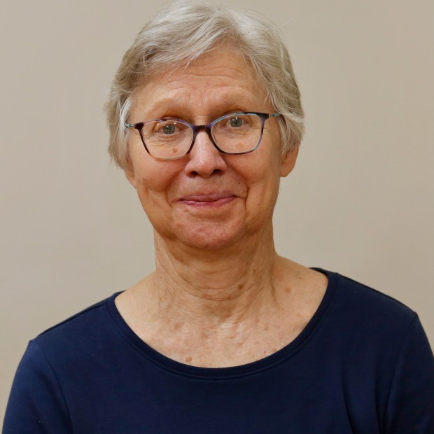 A portrait photo of a light-skinned woman looking directly at the camera. She is wearing glasses and a black top.