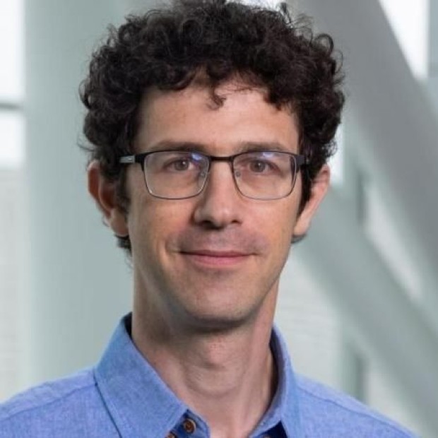 Person with curly hair in a blue collared shirt indoors near large windows.