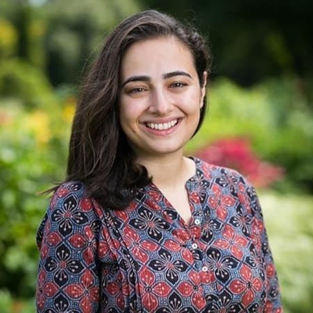 Person in patterned shirt standing in front of green plants.