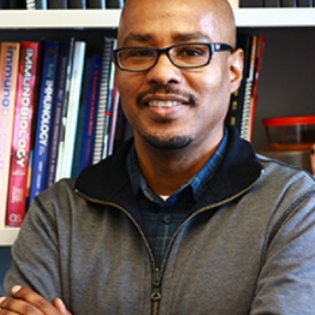 picture of Avery August, wearing glasses and standing in front of a book case