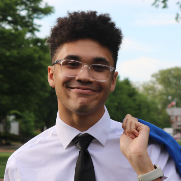 Camron, smiling, glasses, white shirt, black tie, holding a blazer above one shoulder