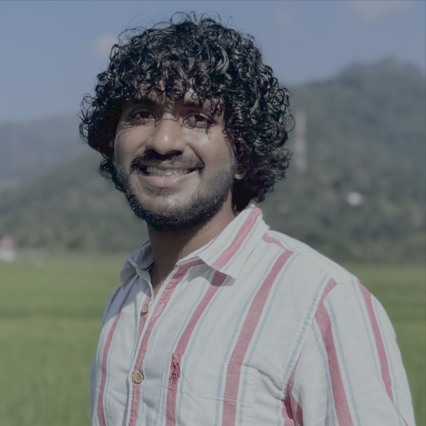 smiling outdoors, green hill in the background; wearing a pink striped shirt