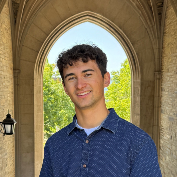 smiling with head titled, wearing navy blue shirt, framed by an archway in the background