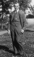 Carl L. Becker standing outside, on grass, one knee slightly bent, trees in background.